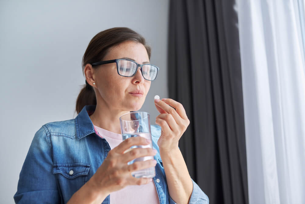 Mature Middle-Aged Woman in Casual Clothes at Home Holding Pill and Glass of Fresh Water. 