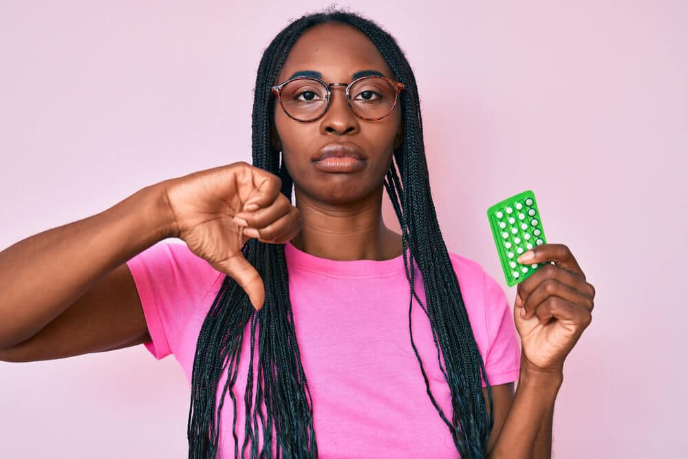 African American Woman With Braids Holding Birth Control Pills With Angry Face, Negative Sign Showing Dislike With Thumbs Down