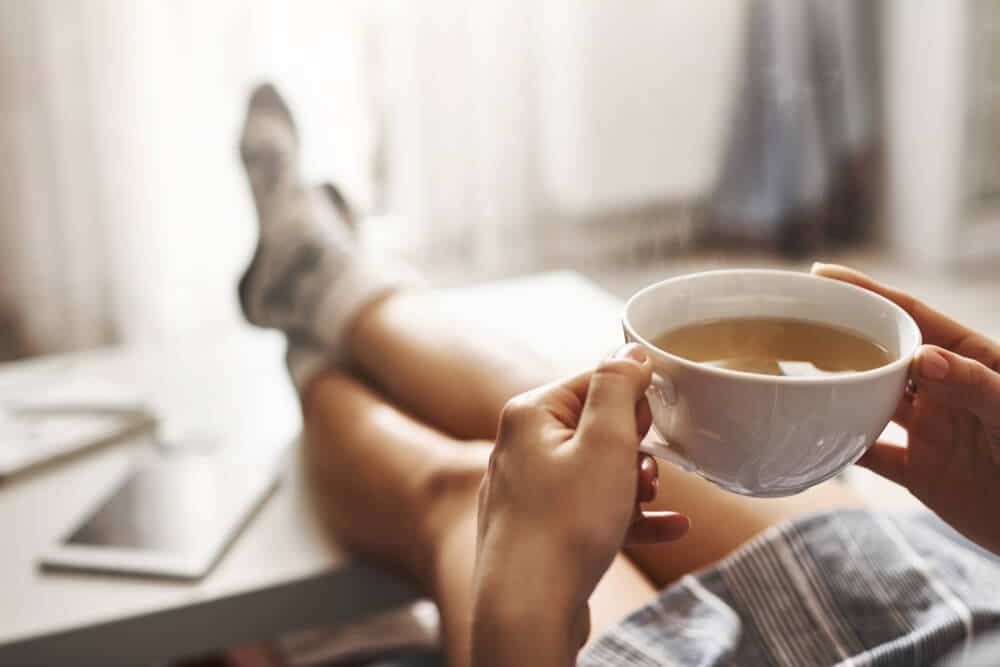 Oman Lying on Couch, Holding Legs on Coffee Table, Drinking Hot Coffee and Enjoying Morning